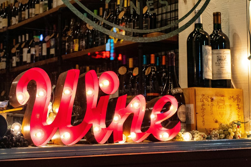 pexels-photo-1374552-1374552 Illuminated wine sign with bottles and grapes create a lively ambiance in a liquor store window.